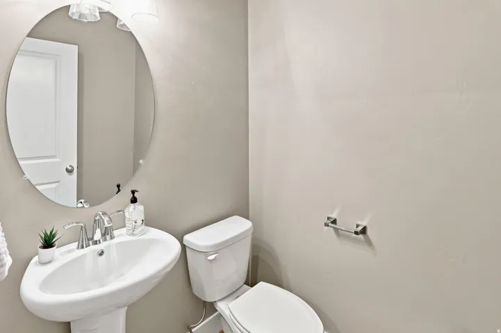 Pedestal sink with chrome faucet, oval mirror, wall-mounted light fixture, and toilet