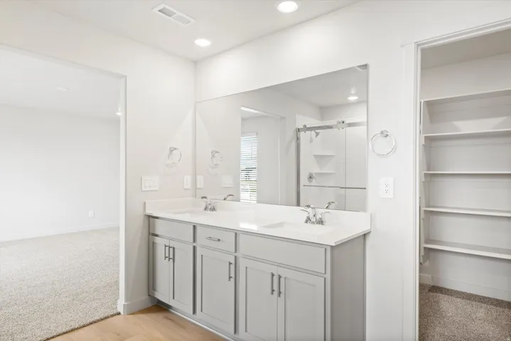 **DISCLAIMER** Interior package may vary. Double vanity with undermount sinks, stone-look countertop, gray cabinetry, and a large wall-mounted mirror
