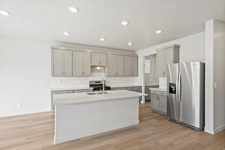 **DISCLAIMER** Interior package may vary. Kitchen featuring wood-finish flooring, recessed lighting, a central island with an integrated sink, a full suite of stainless steel appliances, and light gray cabinetry
