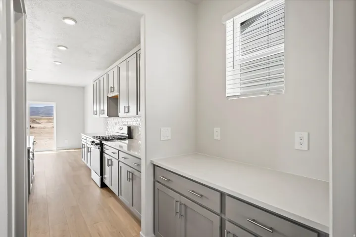**DISCLAIMER** Interior package may vary. Kitchen featuring wood-finish flooring, recessed lighting, white subway tile backsplash, stainless steel range, and gray cabinetry with modern pulls