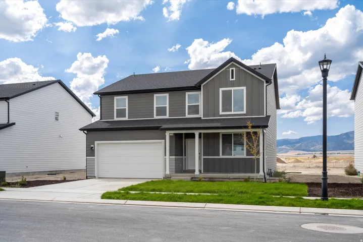 **DISCLAIMER** Exterior package may vary. Two-story residence featuring a dark gray siding exterior, white trim details, an attached garage, a covered front porch, and a landscaped front yard with grass