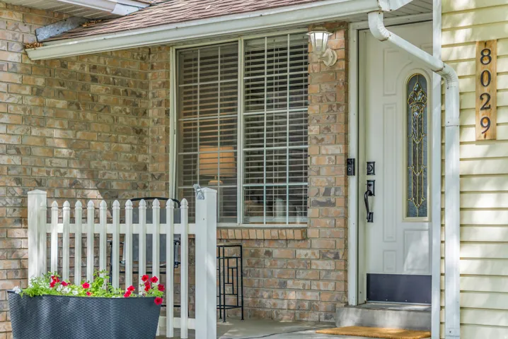 Brick facade with white trim, a white picket fence, and a decorative glass entry door with a black handle