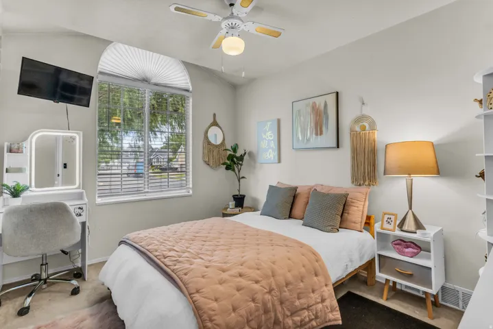 Arched window with blinds, ceiling fan with integrated lighting, wall-mounted television, built-in shelving unit, and neutral wall paint