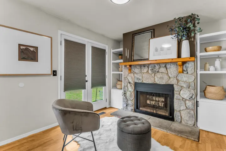 Stone-faced fireplace with a wood mantle, complemented by dual built-in shelving units, light wood-finish flooring, and double glass-paneled doors