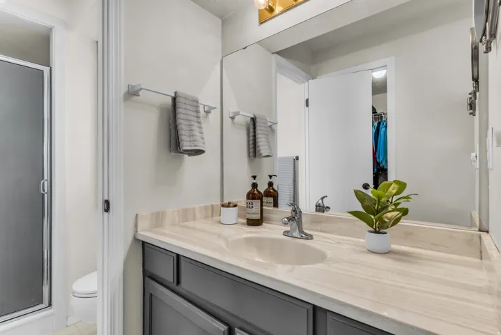 Bathroom featuring a single vanity with an integrated sink, a large mirror, and a shower enclosure with a frosted glass door
