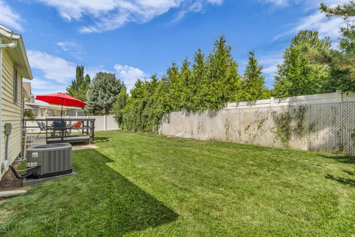 Expansive lawn with a full privacy fence, mature perimeter trees, and an elevated wood deck