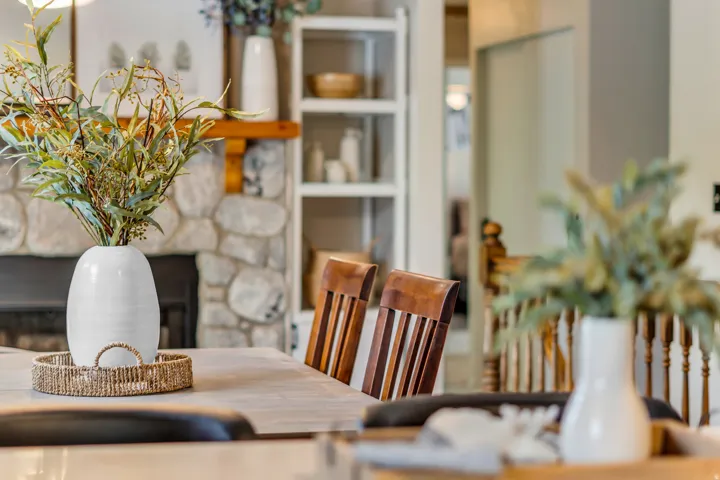 Stone fireplace with a wood mantle, built-in shelving, wood-top dining table, and wood dining chairs