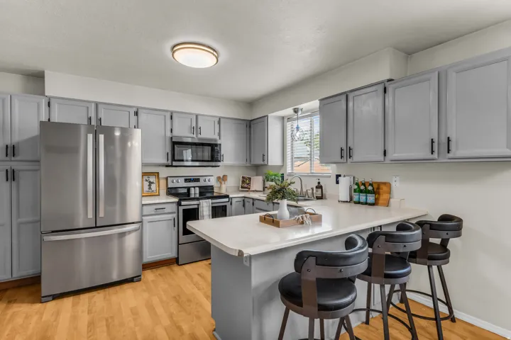 Kitchen featuring light gray cabinetry, stainless steel appliances, light-toned countertops, wood-finish flooring, and a built-in breakfast bar