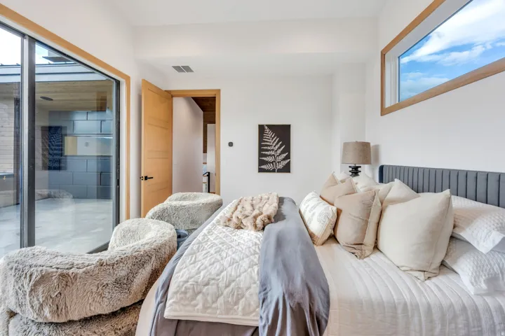 Floor-to-ceiling glass sliding door, horizontal transom window, wood-finish door, white walls, and a gray upholstered headboard