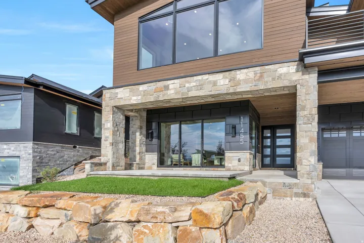Contemporary exterior featuring stone accents, wood-finish siding, expansive windows, a modern entry door, and a two-car garage