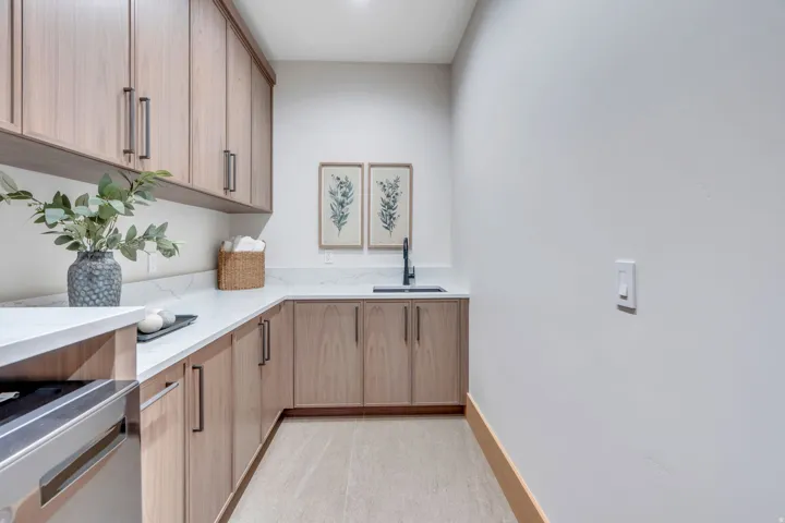 Wood-finish cabinetry with dark hardware, a corner sink with a matte black faucet, white countertops, and light-toned flooring