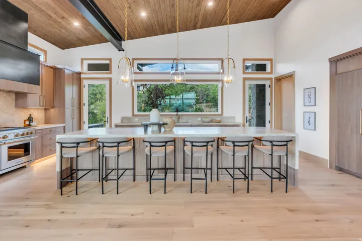 Vaulted wood-paneled ceiling, light wood-finish flooring, custom cabinetry, large kitchen island with seating, and stainless steel range
