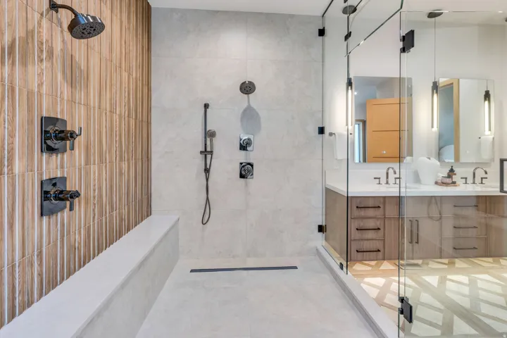 Walk-in shower with wood-finish tile accent wall, multiple shower heads, integrated bench seating, and glass enclosure