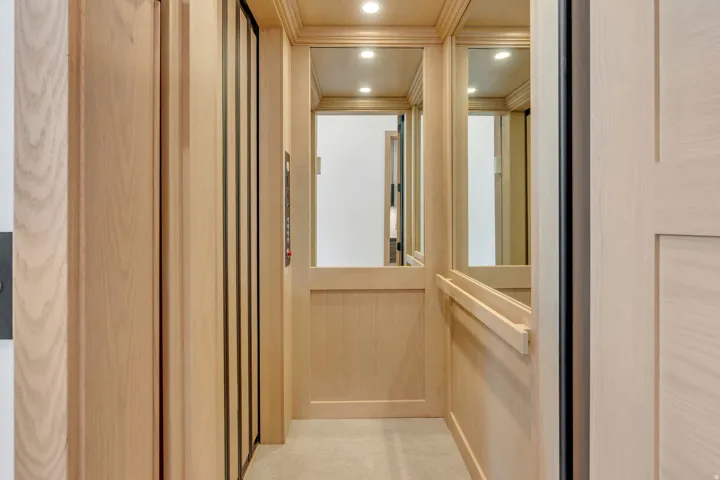 In-home elevator featuring wood paneling, integrated mirrors, recessed lighting, and a grab bar
