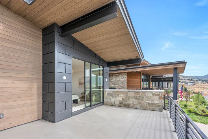 Expansive outdoor deck with wood-finish siding and ceiling, stone-clad wall, black metal railing, and large sliding glass doors