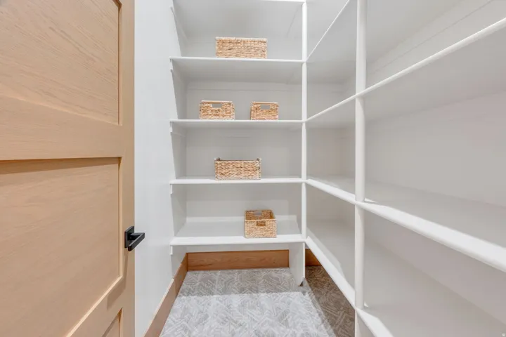 Walk-in pantry featuring extensive white shelving, wood-finish base trim, and patterned flooring