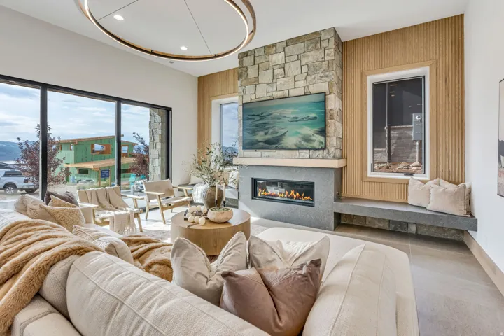 Spacious living area featuring floor-to-ceiling windows, a stone fireplace with a built-in linear electric firebox, a wood panel accent wall, and a built-in stone bench