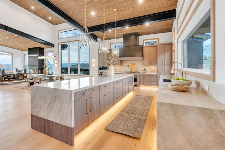 Gourmet kitchen featuring a large waterfall island with integrated lighting, wood-finish flooring, custom cabinetry, and a range hood