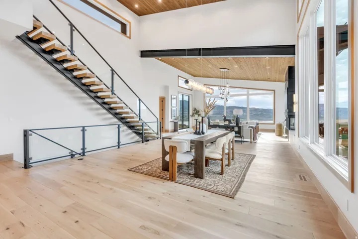 Hardwood flooring, open-tread staircase with glass railing, vaulted wood-paneled ceiling, large picture windows, and integrated wall lighting