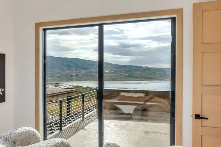Expansive sliding glass door offering mountain and water scenery, with a concrete balcony featuring metal railing