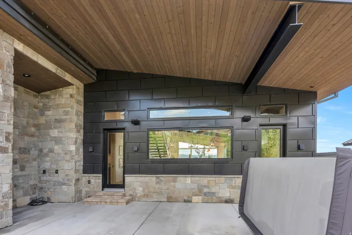 Wood-paneled ceiling with exposed I-beam, stone wall accents, concrete flooring, and multiple windows