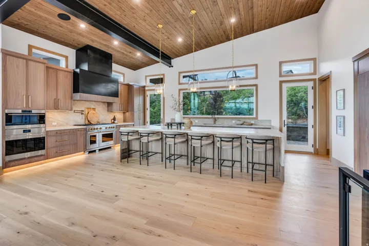 Vaulted wood-paneled ceiling, light wood-finish flooring, custom wood cabinetry, stainless steel appliances, and a large central island with seating