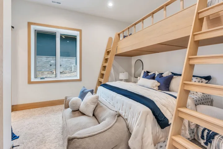 Built-in wooden bunk bed structure, window with wood-finish trim, light-toned carpeting, and white painted walls