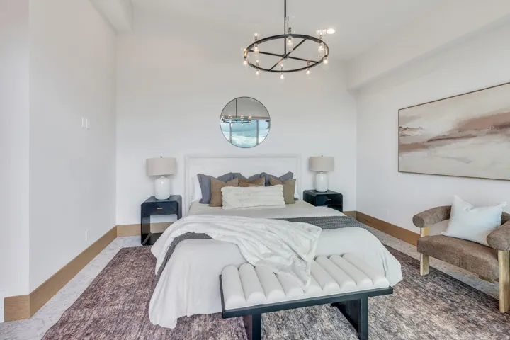 Vaulted ceiling with an overhead chandelier, a white upholstered headboard, and wood-finish flooring