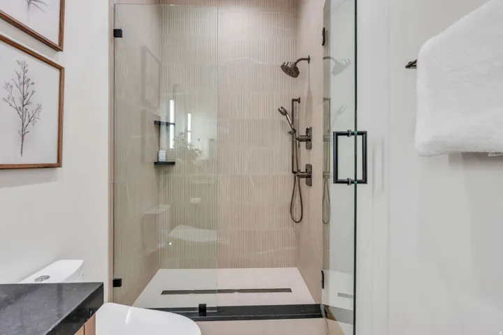 Glass-enclosed shower with a linear drain, matte black fixtures, and textured tile surround