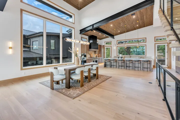 Vaulted wood-finish ceiling, light wood-finish flooring, full-height windows, kitchen island with seating, and open-tread staircase with glass railing
