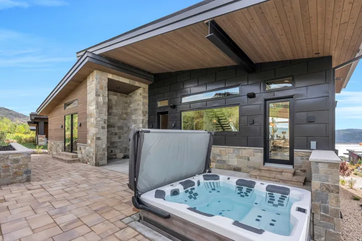 Outdoor spa with cover, paver patio, stone veneer accents, wood-finish soffit, and dark panel siding