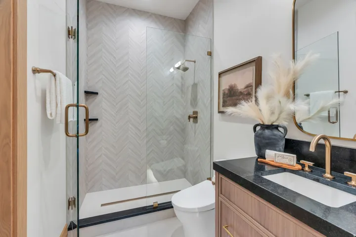 Walk-in shower with herringbone tile, glass enclosure, and brass fixtures