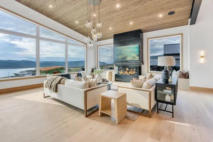 Spacious living area featuring expansive windows, wood-finish flooring, a wood-paneled ceiling, a modern fireplace, and a multi-light pendant chandelier