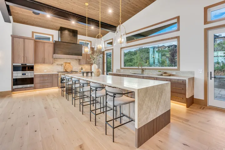 Vaulted wood-paneled ceiling with exposed beams, light wood-finish flooring, custom wood cabinetry, stone countertops, and integrated stainless steel appliances