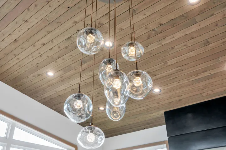 Wood-finish plank ceiling with recessed lighting and a multi-pendant lighting fixture featuring clear glass globes