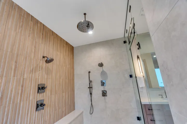Walk-in shower with ceiling-mounted rainfall showerhead, glass enclosure, and textured vertical tile accents