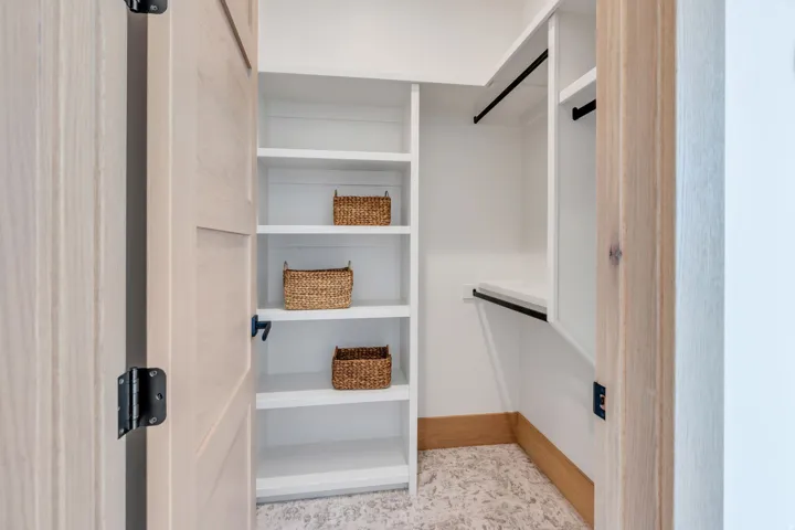 Built-in shelving, white cabinetry, dark hanging rods, wood-finish door, and patterned floor covering