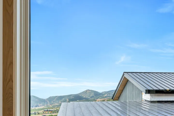Window framing with light wood-finish trim, metal roof, and distant mountainous terrain