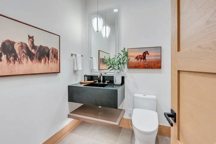 Floating vanity with a dark countertop and integrated sink, modern toilet, and wood-finish door