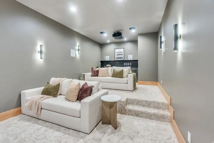 Tiered seating with carpeted steps, integrated projector, recessed ceiling lighting, wall-mounted sconces, and a built-in wet bar with a beverage cooler