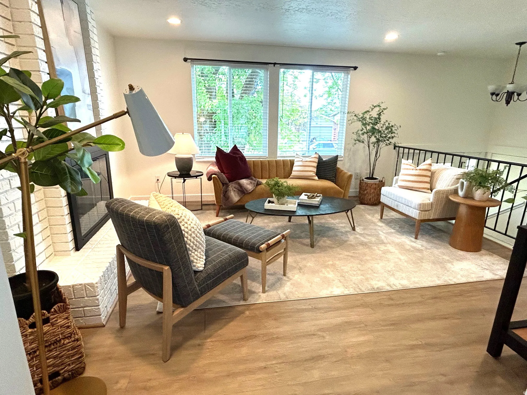 Recessed lighting, light wood-finish flooring, white brick fireplace, black metal railing, and large windows