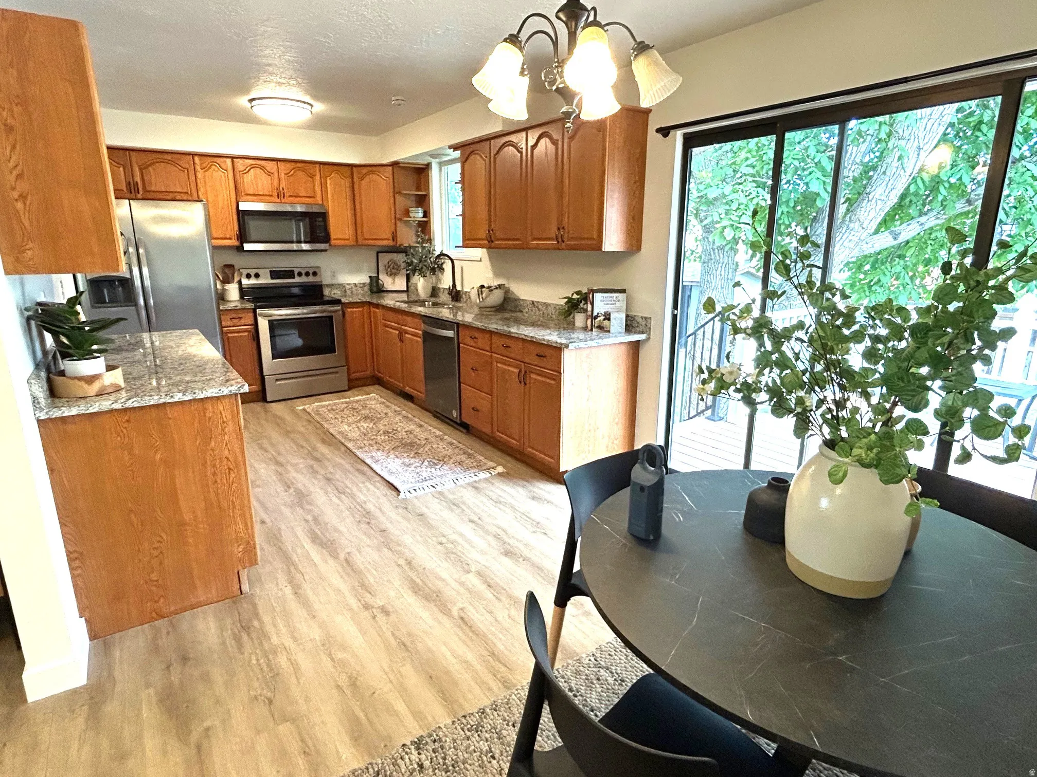 Kitchen featuring wood-finish cabinetry, stainless steel appliances, granite-look countertops, and wood-look flooring