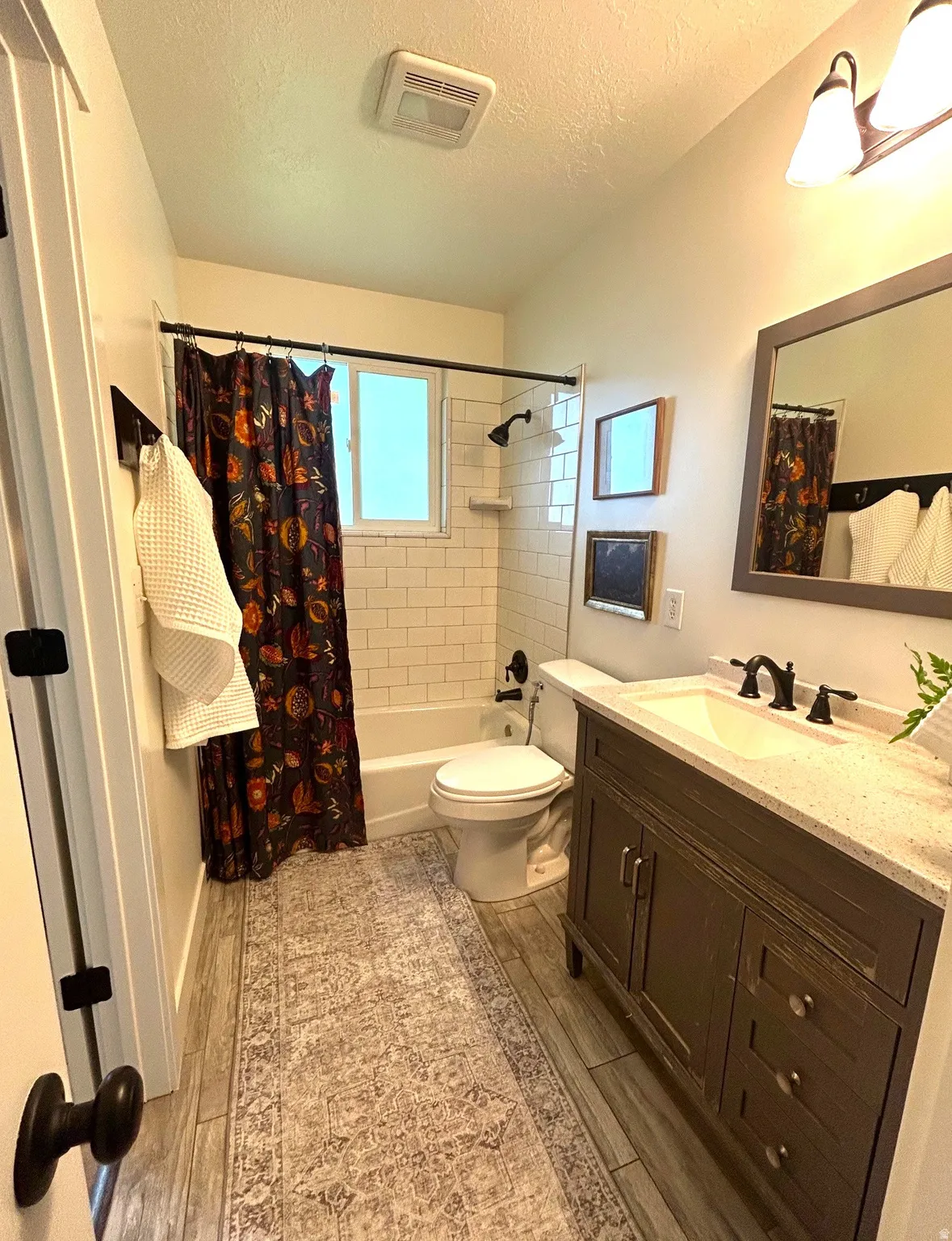 Wood-finish flooring, subway tile shower surround, dark wood vanity with white countertop, integrated sink, and matte black fixtures