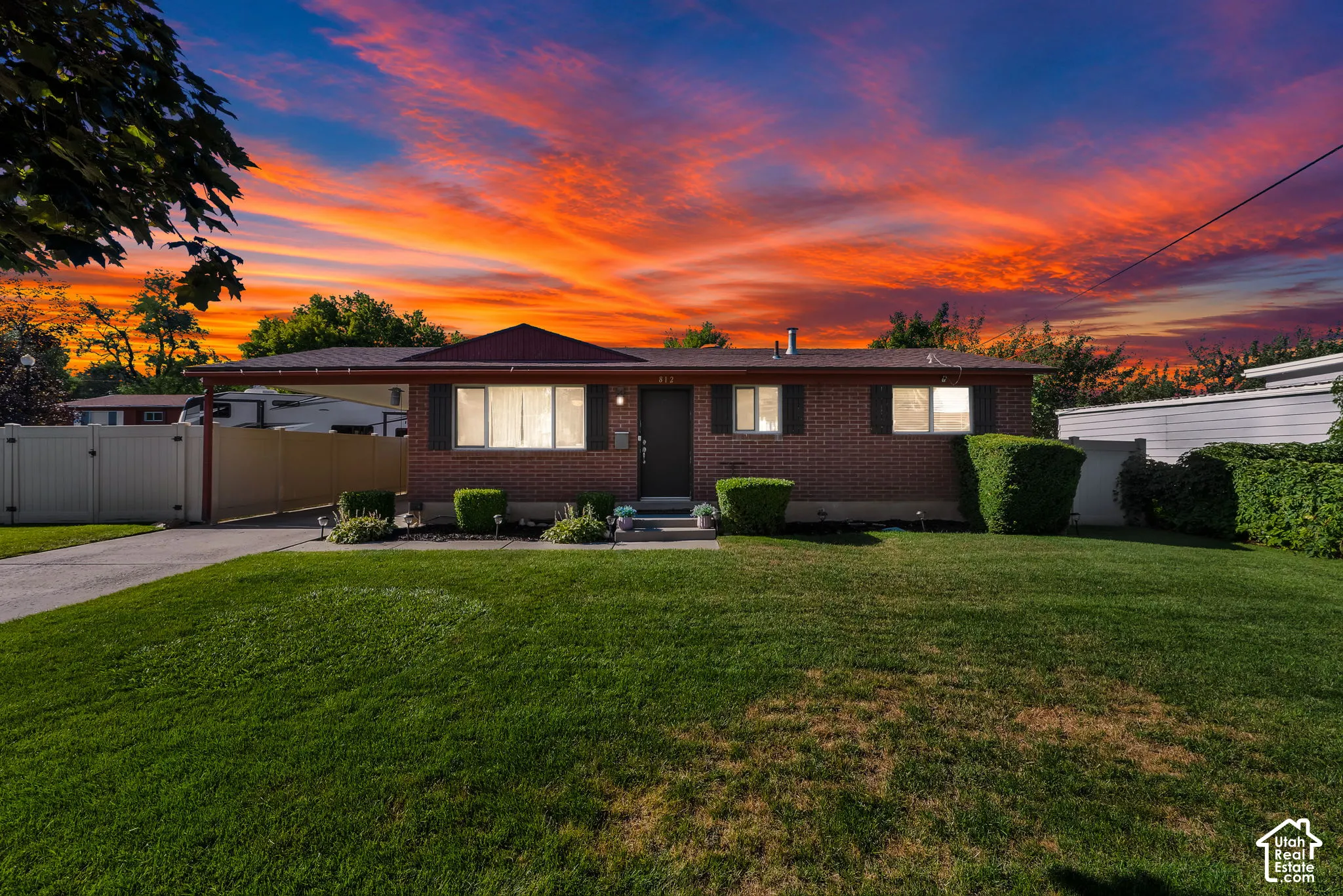 Brick exterior with a carport, front lawn, mature landscaping, and an asphalt driveway