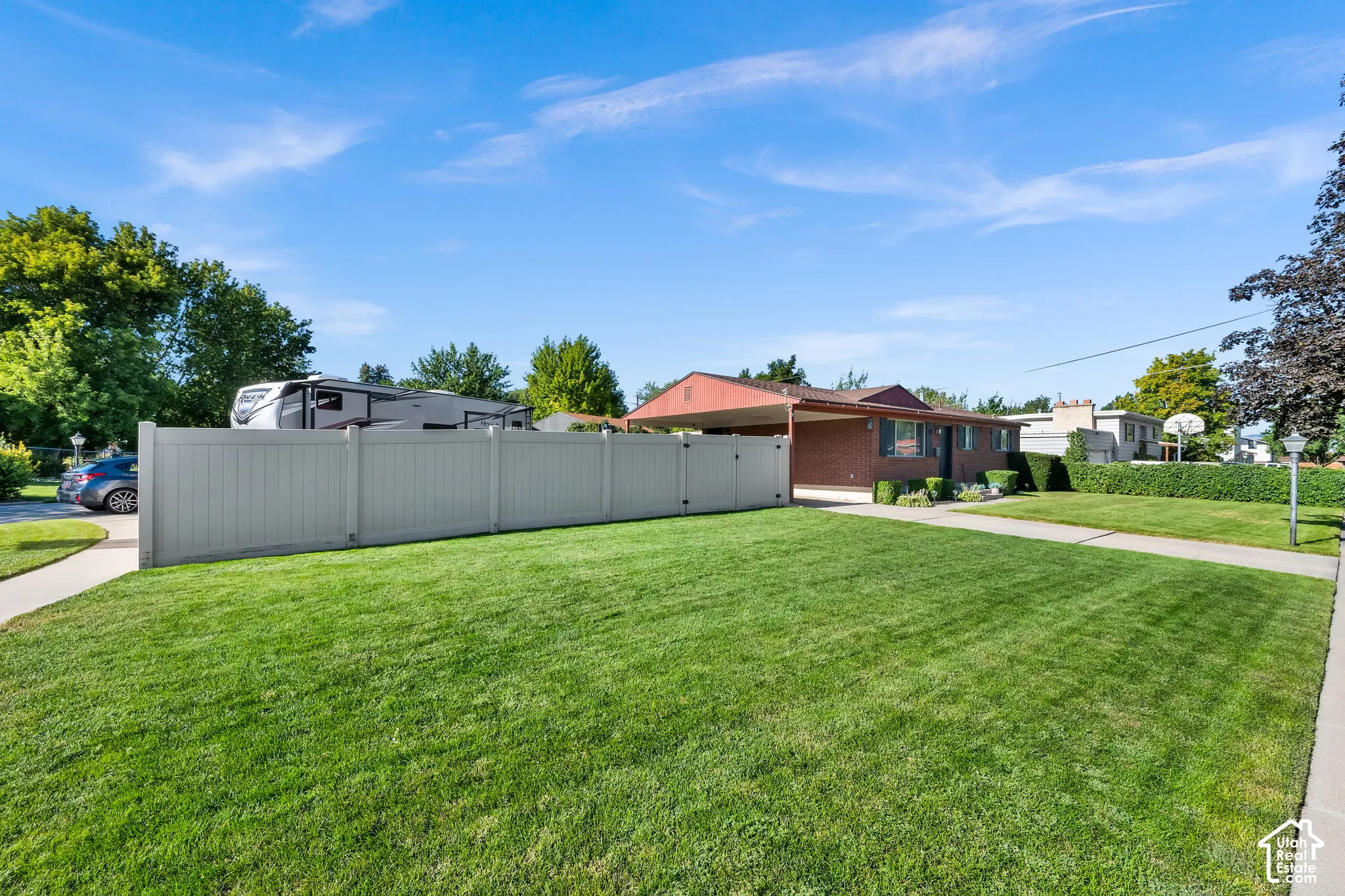 Expansive front yard with a manicured lawn, concrete walkway, and privacy fencing
