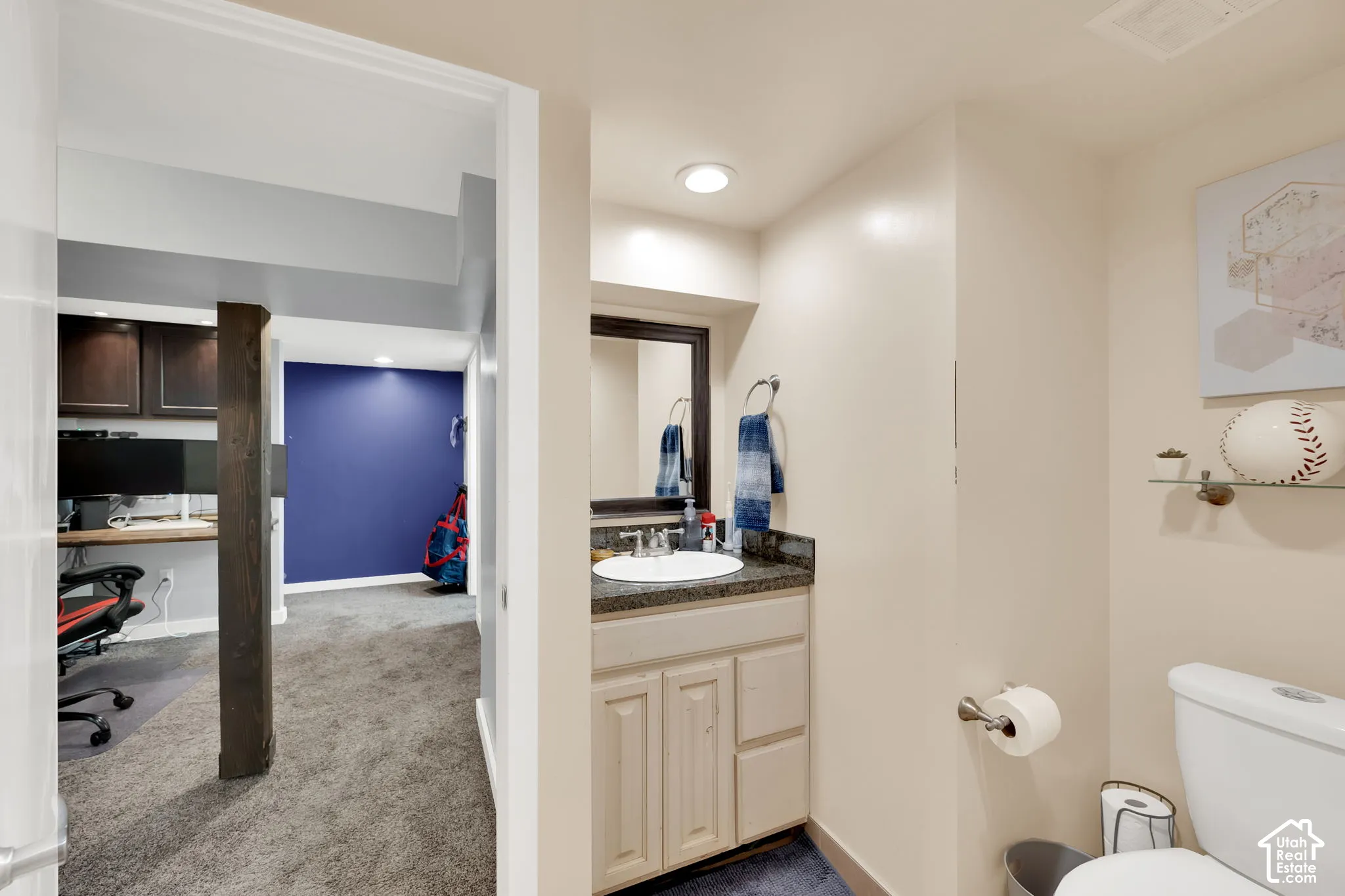 Vanity with integrated sink and dark countertop, recessed lighting, and a built-in wood-finish desk with cabinetry