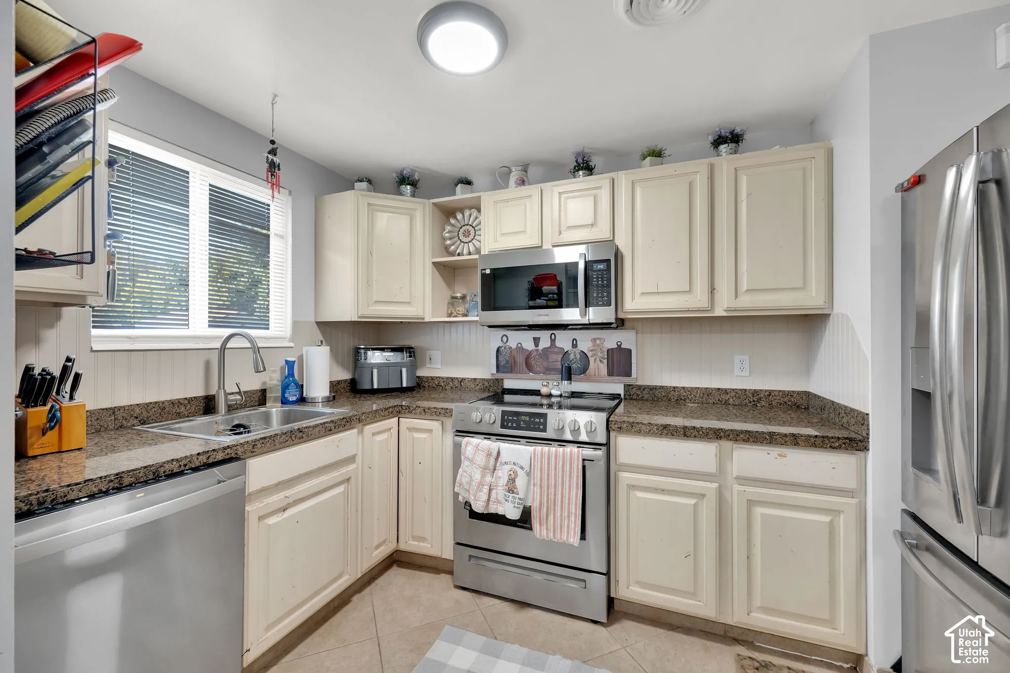 Kitchen featuring light-toned cabinetry, stainless steel appliances, granite-look countertops, a stainless steel sink, and a window with blinds