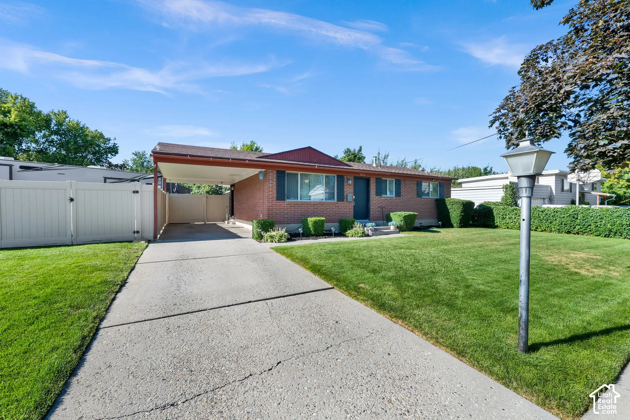 Brick exterior with a covered carport, concrete driveway, and a fenced side yard