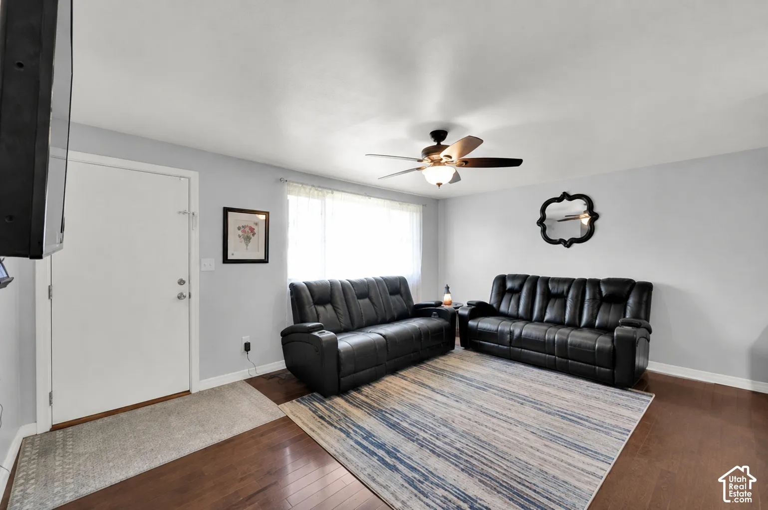 Hardwood flooring, light gray wall paint, large window, ceiling fan with light fixture, and white trim