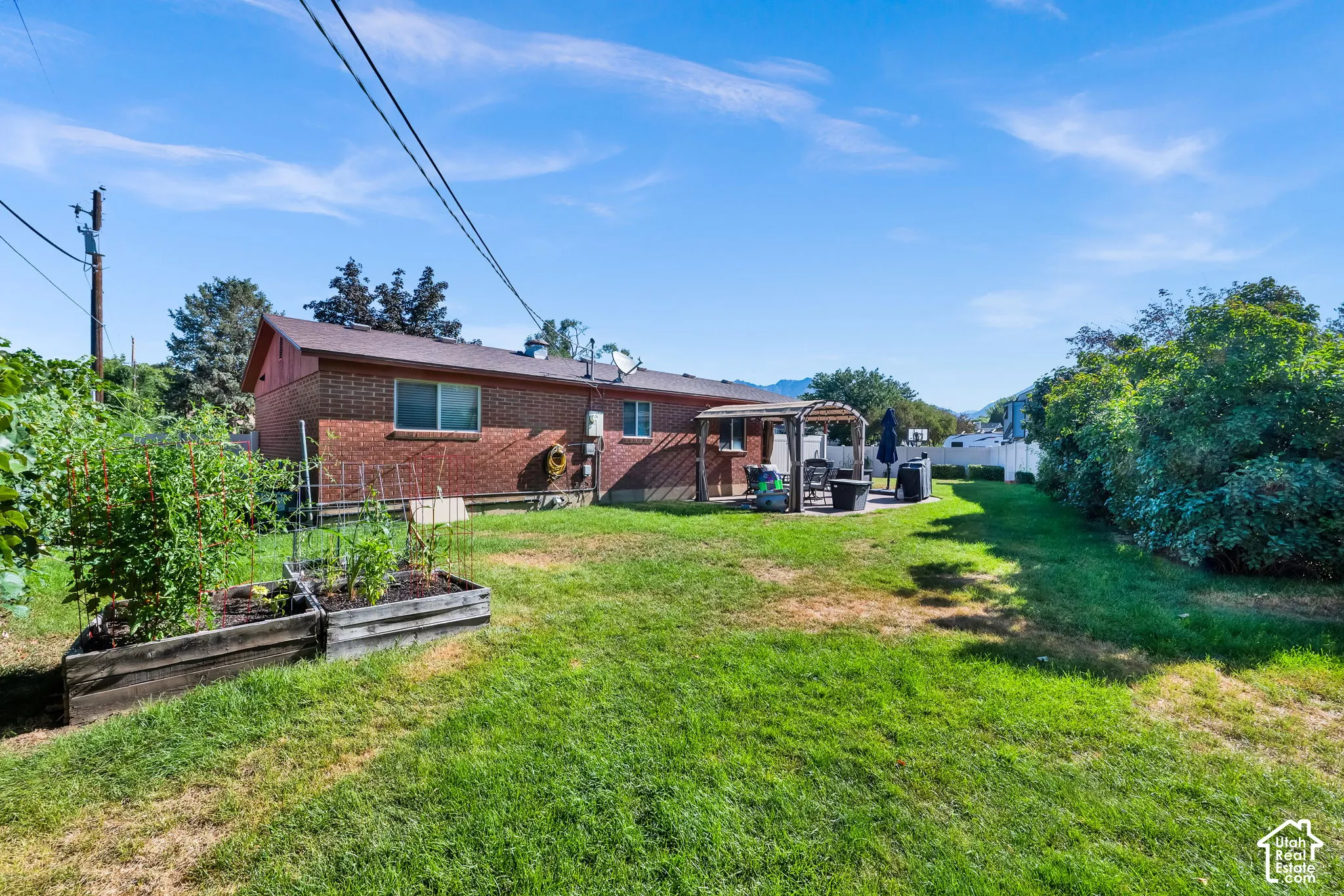 Expansive backyard featuring a brick exterior, a paved patio with a pergola, raised garden beds, and mature perimeter landscaping